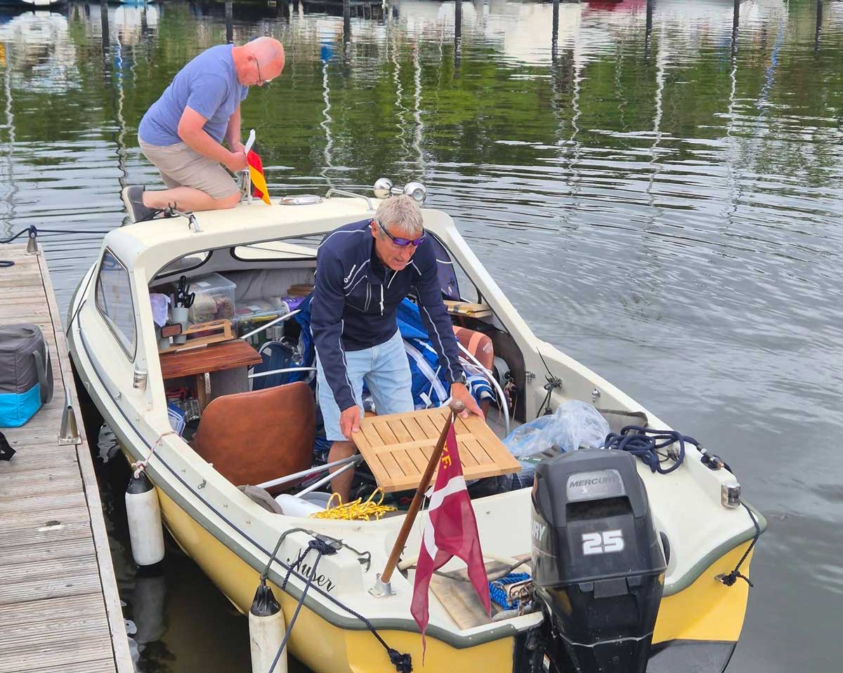 Henrik Bust och Poul Jørgensen flyttar packning i den lilla motorbåten Nuser vid en brygga.